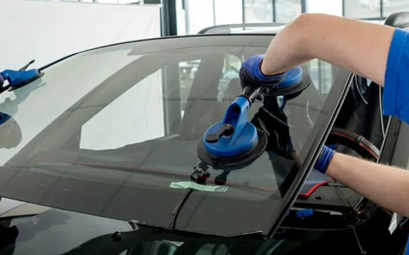 Technician lifting a windshield into place with suction cups